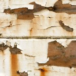 Old white peeling paint on wood, with rust colored tinges.